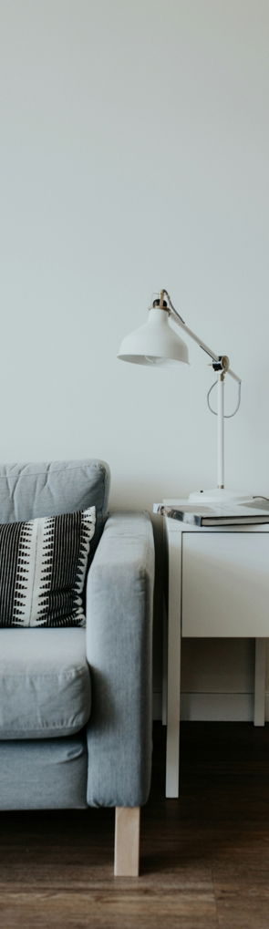 white study lamp on top of white wooden end table beside gray fabric sofa